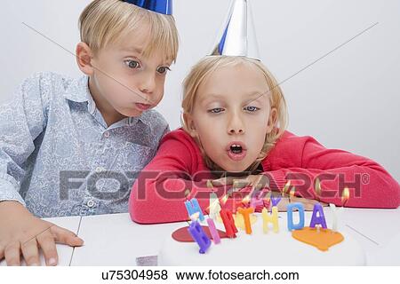 Siblings blowing birthday candles at table View Large Photo Image Stock Photo - Siblings blowing birthday candles at table. Fotosearch