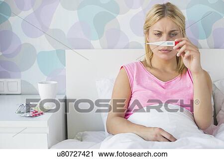 Sick young woman taking temperature with thermometer in bed View Large Photo Image Stock Image - Sick young woman taking temperature with thermometer in bed. Fotosearch