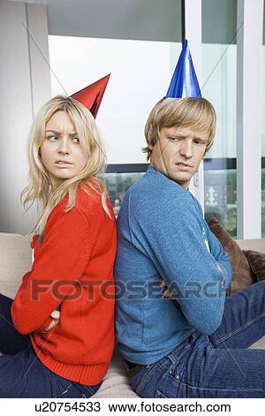Side view of annoyed couple in Christmas sweaters and party hats sitting back to back at home View Large Photo Image Stock Image - Side view of annoyed couple in Christmas sweaters and party hats sitting back to back at home. Fotosearch