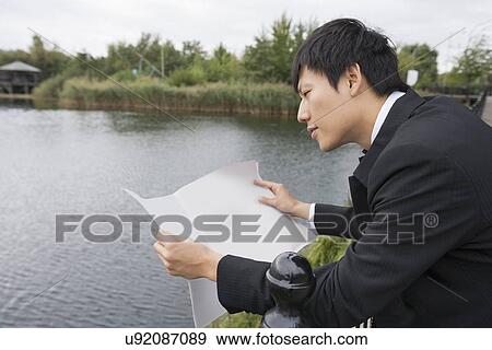 Side view of Asian businessman reading newspaper outside View Large Photo Image Stock Photo - Side view of Asian businessman reading newspaper outside. Fotosearch