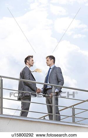 Side view of businessmen shaking hands at terrace railings against sky View Large Photo Image Stock Image - Side view of businessmen shaking hands at terrace railings against sky. Fotosearch