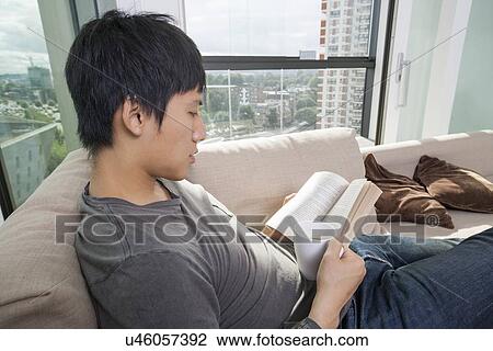 Side view of mid adult man having coffee while reading book on sofa View Large Photo Image Stock Image - Side view of mid adult man having coffee while reading book on sofa. Fotosearch