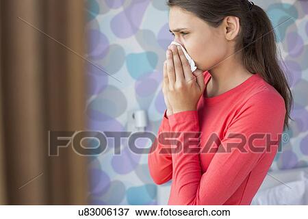Side view of young woman blowing nose at home View Large Photo Image Stock Photo - Side view of young woman blowing nose at home. Fotosearch