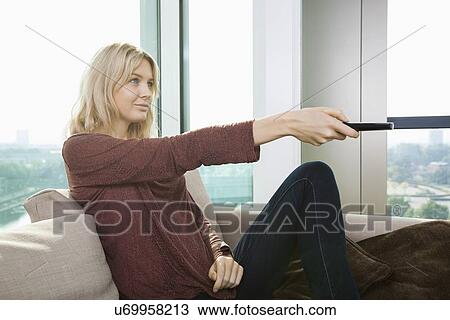 Side view of young woman watching television on sofa at home View Large Photo Image Stock Image - Side view of young woman watching television on sofa at home. Fotosearch