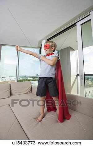 Smiling boy in super hero costume standing with arm outstretched on sofa bed at home View Large Photo Image Stock Image - Smiling boy in super hero costume standing with arm outstretched on sofa bed at home. Fotosearch