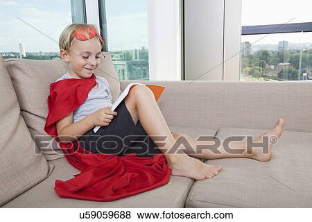 Smiling boy in superhero costume reading book on sofa at home View Large Photo Image Stock Photo - Smiling boy in superhero costume reading book on sofa at home. Fotosearch