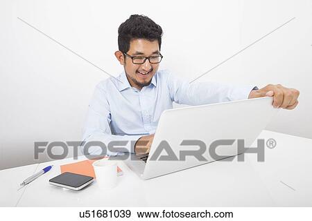 Stock Photo - Smiling businessman working on laptop at desk in office. Fotosearch