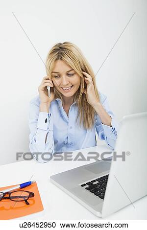 Stock Image - Smiling businesswoman answering cell phone in office. Fotosearch