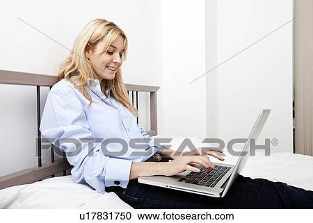 Stock Image - Smiling businesswoman using laptop in bed. Fotosearch