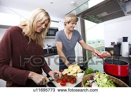 Stock Image - Smiling Caucasian couple cooking together in kitchen. Fotosearch