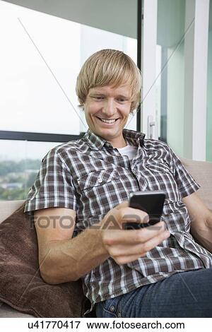 Smiling mid-adult man text messaging on sofa at home View Large Photo Image Stock Photo - Smiling mid-adult man text messaging on sofa at home. Fotosearch