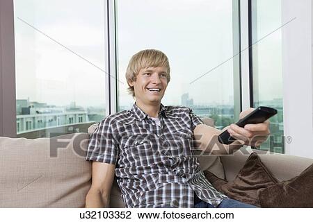 Smiling mid-adult man watching television on sofa at home View Large Photo Image Stock Image - Smiling mid-adult man watching television on sofa at home. Fotosearch