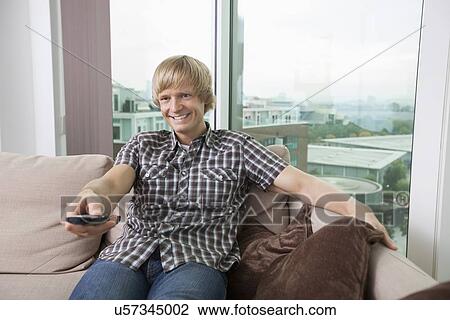 Smiling mid-adult man watching television on sofa at home View Large Photo Image Stock Image - Smiling mid-adult man watching television on sofa at home. Fotosearch