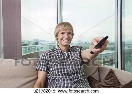 Smiling mid-adult man watching television on sofa at home View Large Photo Image Stock Photography - Smiling mid-adult man watching television on sofa at home. Fotosearch