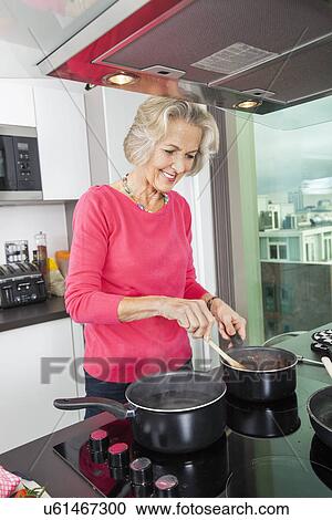 Smiling senior woman preparing food at kitchen counter View Large Photo Image Stock Image - Smiling senior woman preparing food at kitchen counter. Fotosearch