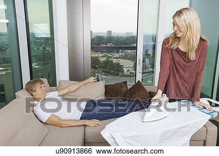 Smiling woman looking at relaxed while ironing shirt in living room at home View Large Photo Image Stock Photograph - Smiling woman looking at relaxed while ironing shirt in living room at home. Fotosearch