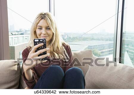 Stock Image - Smiling young woman reading text message at home. Fotosearch
