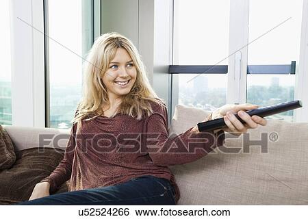 Smiling young woman watching television on sofa at home View Large Photo Image Stock Photograph - Smiling young woman watching television on sofa at home. Fotosearch