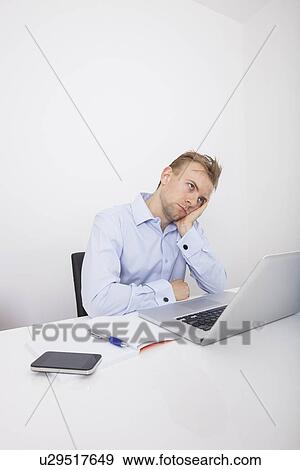 Stressed businessman with laptop sitting at desk in office View Large Photo Image Stock Photo - Stressed businessman with laptop sitting at desk in office. Fotosearch