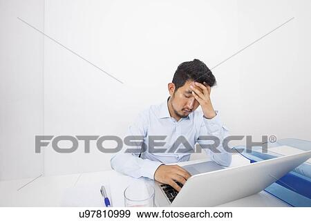 Stock Photo - Stressed businessman with laptop sitting at desk in office. Fotosearch