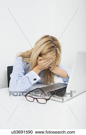 Stock Image - Stressed businesswoman with laptop at office desk. Fotosearch