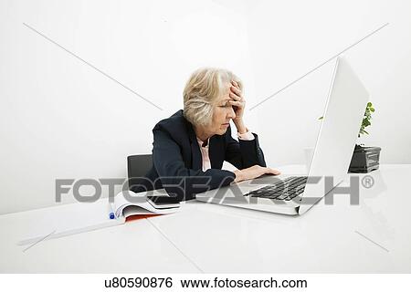 Stock Photograph - Stressed senior businesswoman using laptop at desk in office. Fotosearch