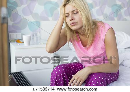 Stressed woman suffering from headache sitting on bed at home View Large Photo Image Picture - Stressed woman suffering from headache sitting on bed at home. Fotosearch