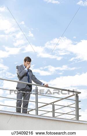 Stressed young businessman rubbing eyes on terrace against sky View Large Photo Image Stock Photograph - Stressed young businessman rubbing eyes on terrace against sky. Fotosearch