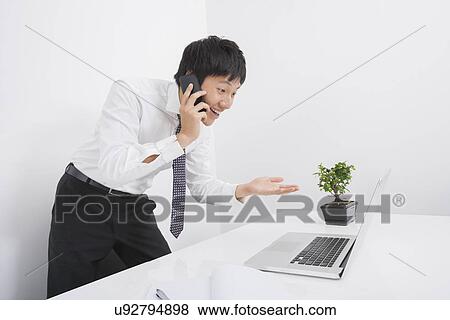 Stock Photo - Surprise businessman using cell phone and laptop in office. Fotosearch