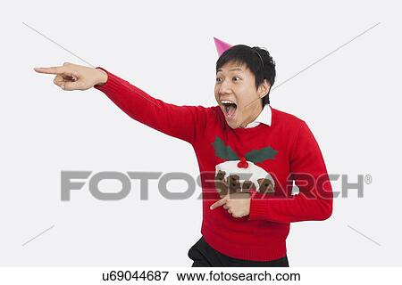 Stock Photo - Surprised man wearing Christmas sweater while pointing over white background. Fotosearch