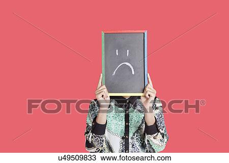 Teenage boy holding slate with sad smiley on it over red background View Large Photo Image Stock Image - Teenage boy holding slate with sad smiley on it over red background. Fotosearch