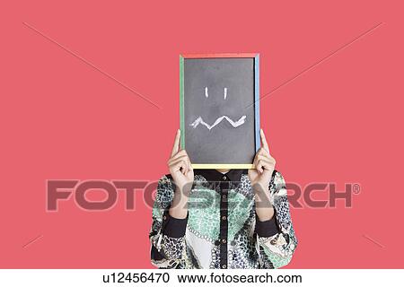 Teenage boy holding slate with confusion smiley on it over red background View Large Photo Image Stock Image - Teenage boy holding slate with confusion smiley on it over red background. Fotosearch