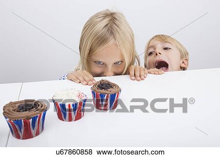 Tempted children looking at cupcakes on table View Large Photo Image Stock Photo - Tempted children looking at cupcakes on table. Fotosearch