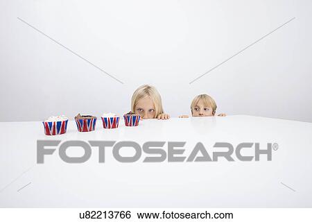 Stock Photograph - Tempted children staring at cupcakes on table. Fotosearch