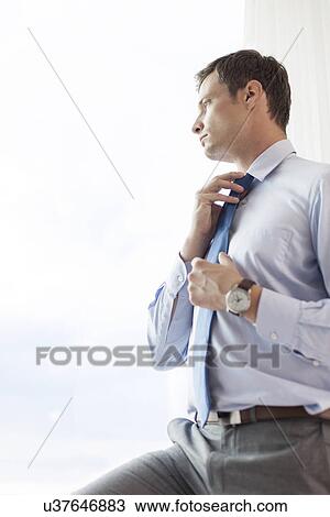 Thoughtful businessman adjusting necktie in hotel View Large Photo Image Stock Image - Thoughtful businessman adjusting necktie in hotel. Fotosearch