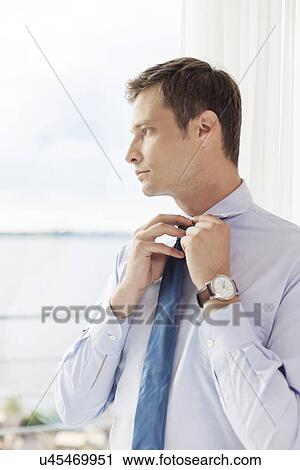 Stock Image - Thoughtful businessman adjusting necktie in hotel. Fotosearch