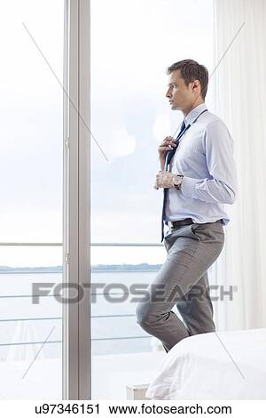 Thoughtful businessman adjusting necktie in hotel View Large Photo Image Stock Image - Thoughtful businessman adjusting necktie in hotel. Fotosearch