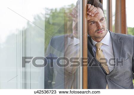 Thoughtful businessman looking away while leaning on glass door View Large Photo Image Stock Image - Thoughtful businessman looking away while leaning on glass door. Fotosearch