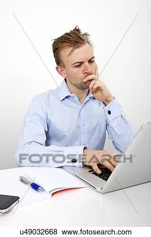Thoughtful businessman using laptop at desk in office View Large Photo Image Stock Photo - Thoughtful businessman using laptop at desk in office. Fotosearch