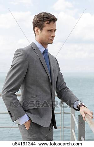 Thoughtful businessman with hand in pocket standing by terrace railings View Large Photo Image Picture - Thoughtful businessman with hand in pocket standing by terrace railings. Fotosearch