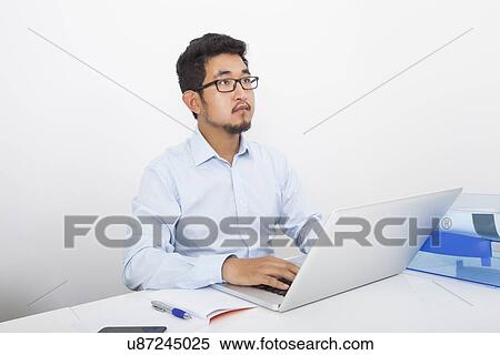 Thoughtful businessman with laptop sitting at desk in office View Large Photo Image Stock Photography - Thoughtful businessman with laptop sitting at desk in office. Fotosearch