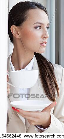 Stock Photo - Thoughtful businesswoman having coffee in office. Fotosearch