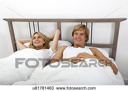 Stock Image - Thoughtful couple lying in bed at home. Fotosearch