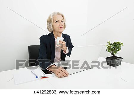 Thoughtful senior businesswoman having coffee at desk in office View Large Photo Image Stock Image - Thoughtful senior businesswoman having coffee at desk in office. Fotosearch