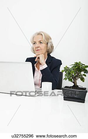 Thoughtful senior businesswoman with laptop sitting at desk in office View Large Photo Image Stock Photograph - Thoughtful senior businesswoman with laptop sitting at desk in office. Fotosearch