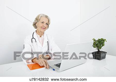 Thoughtful senior female doctor with laptop at desk in clinic View Large Photo Image Stock Image - Thoughtful senior female doctor with laptop at desk in clinic. Fotosearch