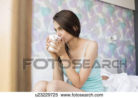 Stock Photography - Thoughtful young woman drinking coffee in bedroom. Fotosearch