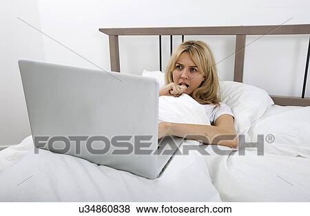 Thoughtful young woman looking at laptop in bed View Large Photo Image Stock Photo - Thoughtful young woman looking at laptop in bed. Fotosearch