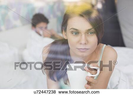 Thougtful woman having coffee at home with man lying in background View Large Photo Image Stock Photo - Thougtful woman having coffee at home with man lying in background. Fotosearch