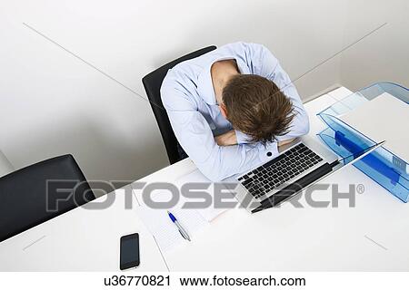 Stock Image - Tired businessman sleeping on laptop at desk in office. Fotosearch